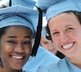 Two graduates wearing regalia smile at the camera